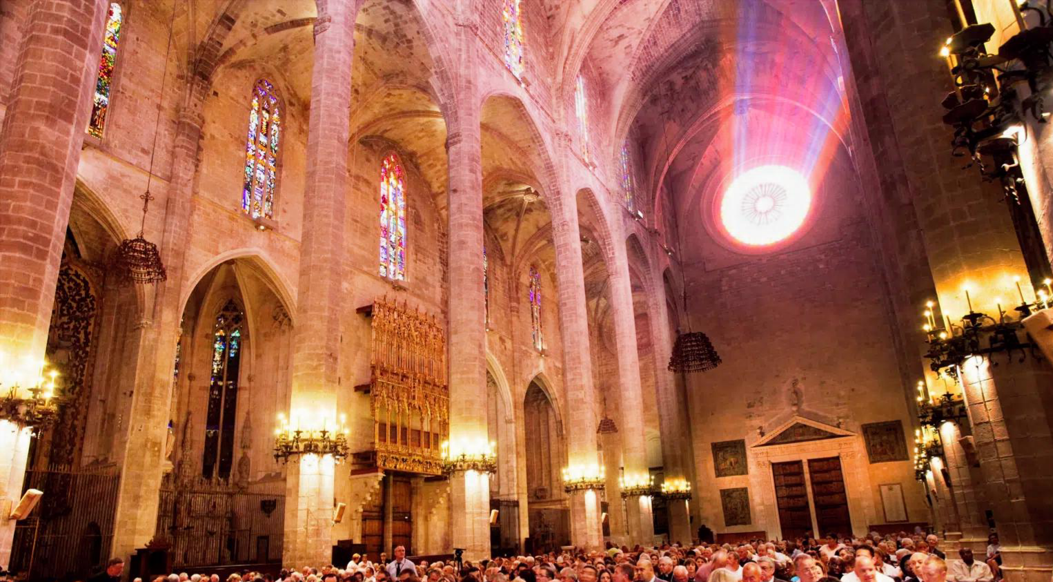 The interior of La Seu, the Cathedral of Palma, with a beam of stained-glass light falling over the audience on the night of the premiere